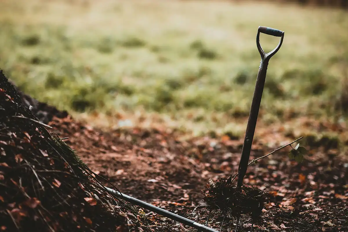 Sturdy compost shovel being used for organic waste management in backyard compost heap.